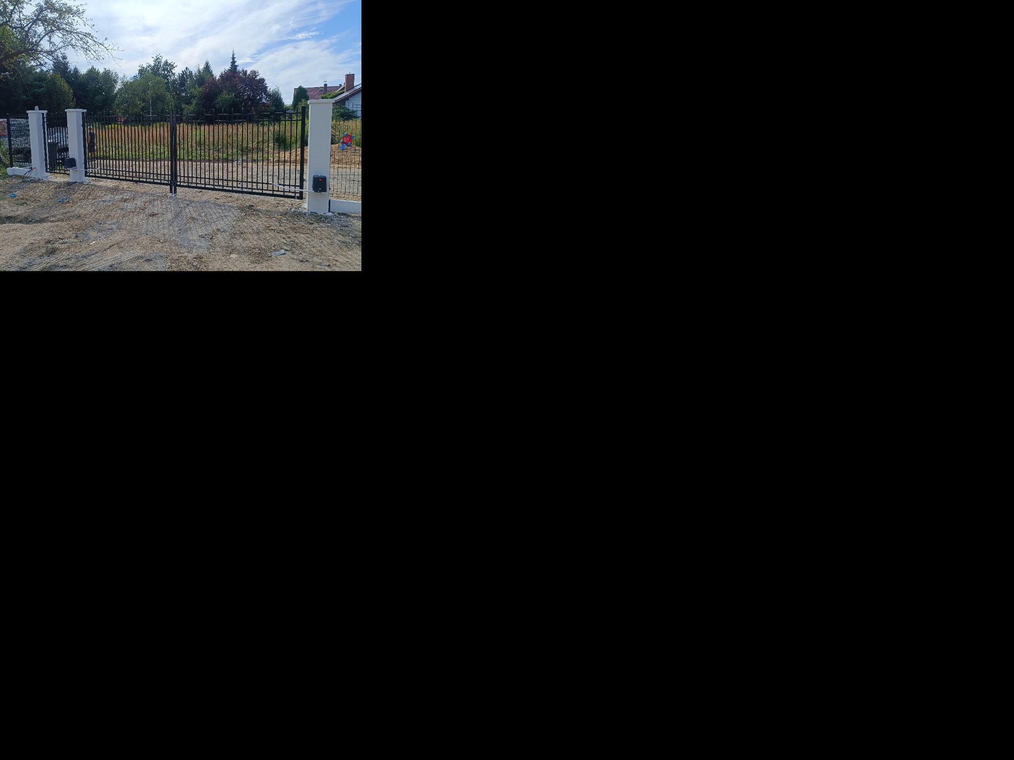 Czarna brama wjazdowa z automatyką, osadzona na betonowych słupkach w Przytkowicach. Widoczne elementy montażowe i teren przygotowany pod dalsze prace.