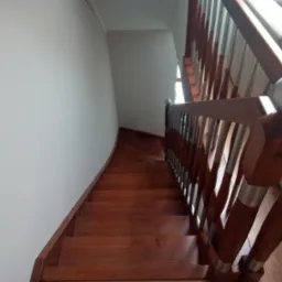 Wysoki kąt widzenia na drewniane schody z poręczą z metalowymi elementami, prowadzące w górę w jasnym wnętrzu.