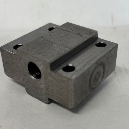 MAGMA Tech - Szary, metalowy element z otworami po precyzyjnej obróbce, widoczne ślady frezowania. Detal na jasnym tle, ostre światło podkreśla fakturę metalu.