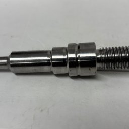 MAGMA Tech - Metalowy, precyzyjnie wykonany element z gwintem, prawdopodobnie wytoczony, leżący na białym tle. Widoczne ślady obróbki.