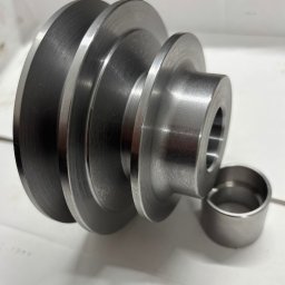 MAGMA Tech - Metalowa, trójstopniowa rolka pasowa z tuleją, precyzyjnie obrobiona. Widoczne ślady po obróbce skrawaniem. Detal gotowy do montażu, leży na białym tle.