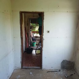 Paweł Stanek - Pokój w trakcie remontu: ściany z widocznymi śladami prac, gruz na podłodze, narzędzia. Widoczne usunięte fragmenty tynku i przygotowanie do dalszych prac wykończeniowych.