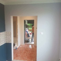 Paweł Stanek - Wnętrze w trakcie odświeżania: pomalowane ściany na szaro i granatowo, fragment mozaiki, widoczny pracownik w przejściu. Podłoga częściowo wyłożona płytkami.