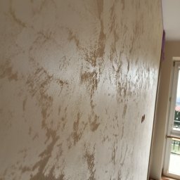 Paweł Stanek - Ściana z dekoracyjną, beżową fakturą, widoczna z boku, z fragmentem okna w tle. Efektowna technika malarska, podkreślona przez delikatne światło.