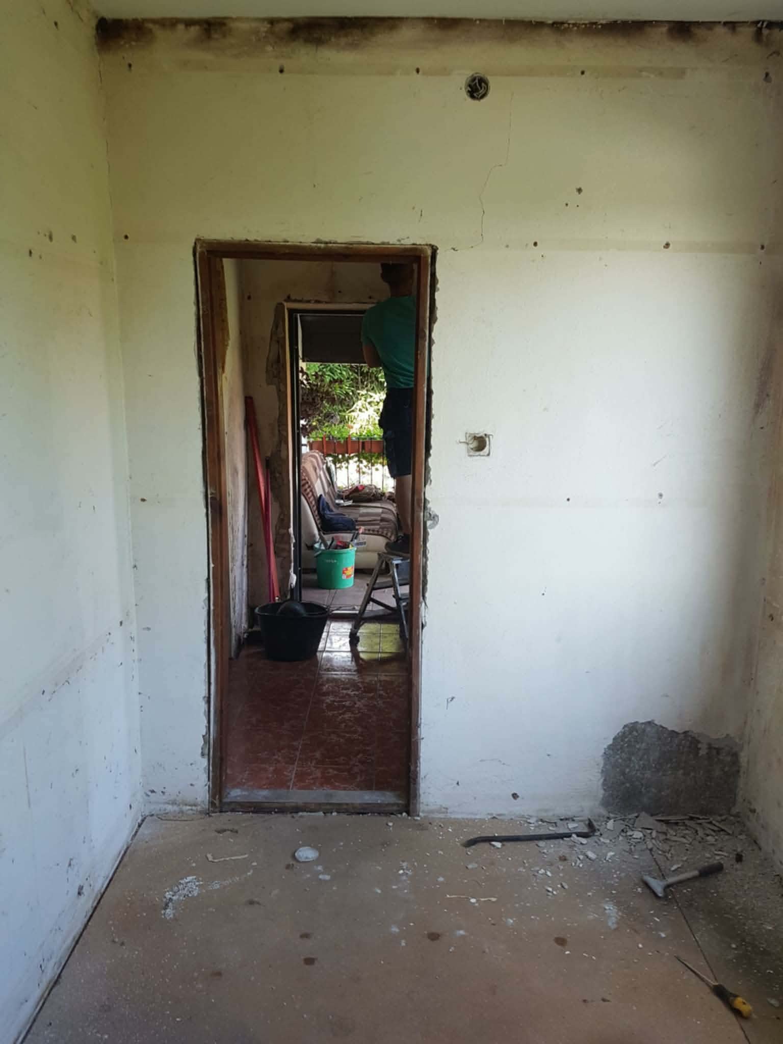 Pokój w trakcie remontu: ściany z widocznymi śladami prac, gruz na podłodze, narzędzia. Widoczne usunięte fragmenty tynku i przygotowanie do dalszych prac wykończeniowych.