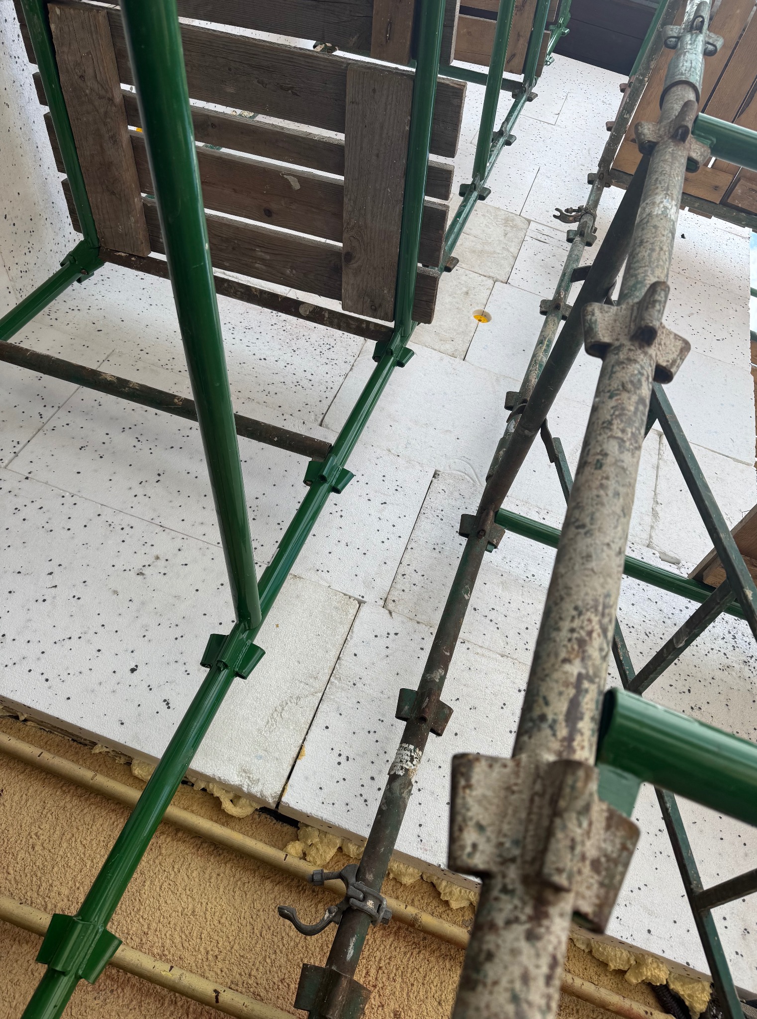 Ocieplanie budynku z użyciem styropianu, widoczne rusztowanie w kolorze zielonym i szarym. Prace na wysokości, widok z dołu. Detal prac wykończeniowych.