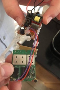 Rozłożony moduł elektroniczny z widocznymi elementami i przewodami, trzymany w dłoniach. Układ scalony z bliska, detale połączeń.