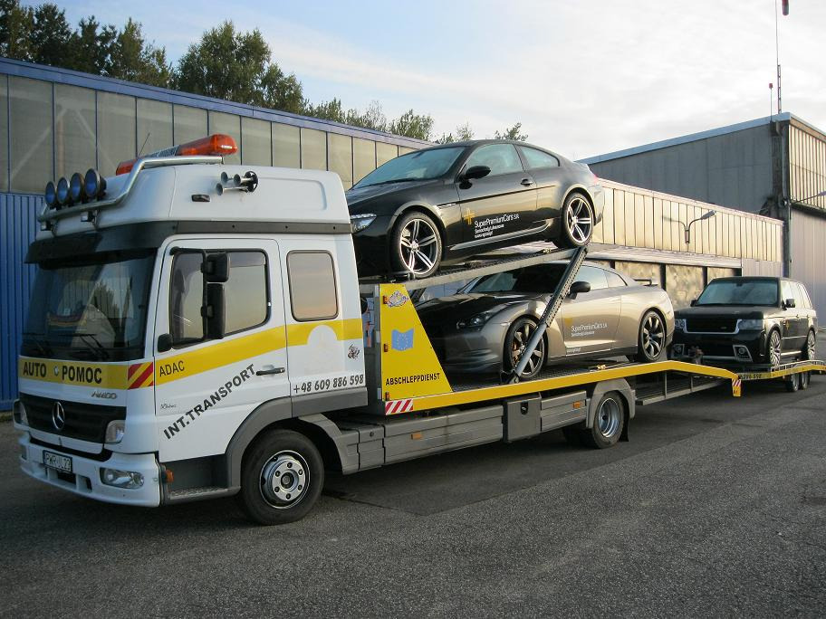 Laweta Mercedes-Benz z trzema luksusowymi autami: czarnym BMW, srebrnym Camaro i czarnym Range Roverem. Widoczne logo firmy transportowej i numer telefonu.