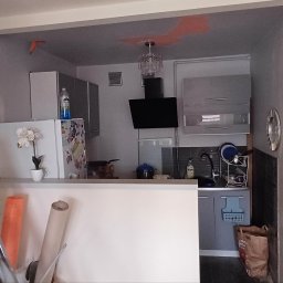 Finish - Kuchnia w trakcie remontu: widoczne ślady malowania na ścianach, drabina malarska z akcesoriami, częściowo umeblowana przestrzeń kuchenna z oświetleniem.