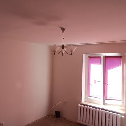 Finish - Jasne wnętrze po malowaniu ścian na gładko, z widocznym oknem z różowymi roletami i klasycznym żyrandolem. Ściany w odcieniach bieli i beżu.