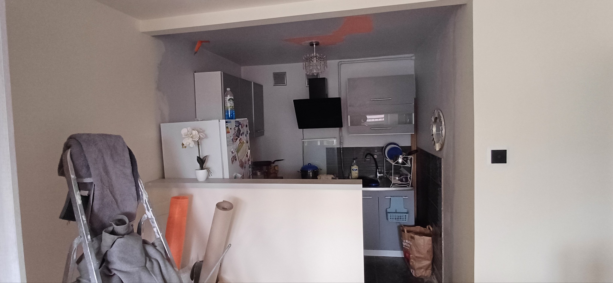 Kuchnia w trakcie remontu: widoczne ślady malowania na ścianach, drabina malarska z akcesoriami, częściowo umeblowana przestrzeń kuchenna z oświetleniem.