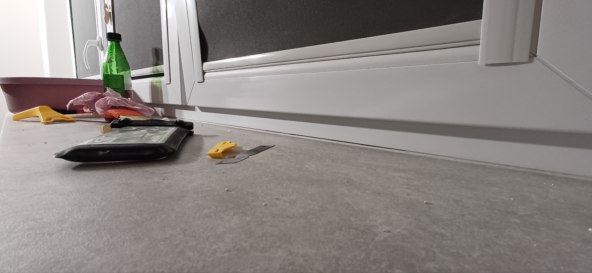 Przygotowanie do prac wykończeniowych przy oknie: narzędzia, butelka i ściereczki na blacie. Widoczne ślady po szpachlowaniu lub malowaniu.