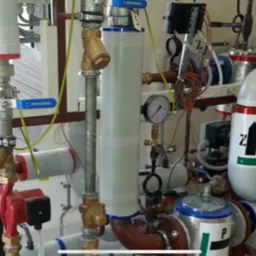 Złożona instalacja hydrauliczna z rurami, zaworami i pompami, widoczne manometry i elementy sterujące, całość zamontowana na metalowej ramie w pomieszczeniu technicznym.