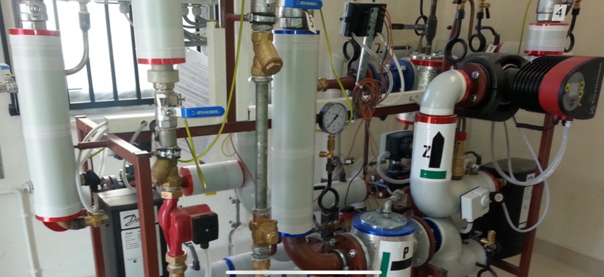 Złożona instalacja hydrauliczna z rurami, zaworami i pompami, widoczne manometry i elementy sterujące, całość zamontowana na metalowej ramie w pomieszczeniu technicznym.