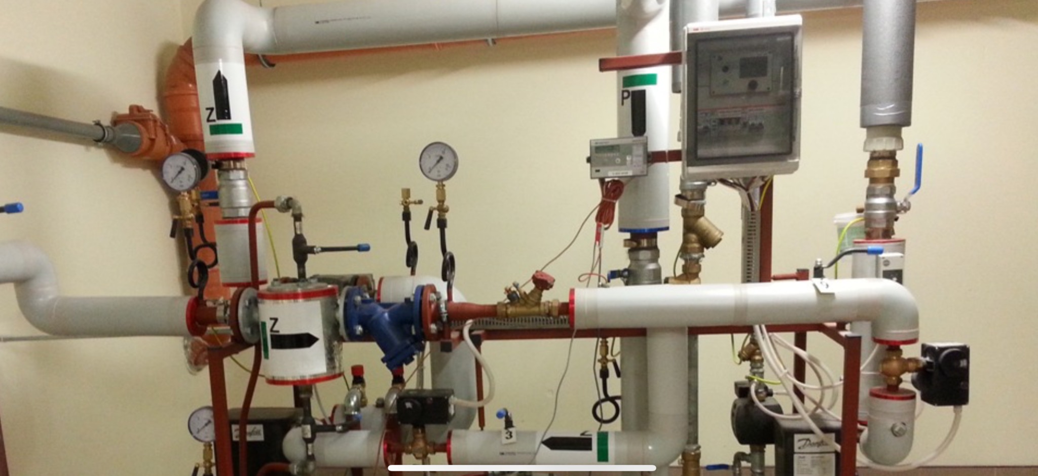 Kompleksowa instalacja rur i zaworów w kotłowni, z widocznymi manometrami, filtrami i elementami sterującymi. Różne materiały i kolory rur.