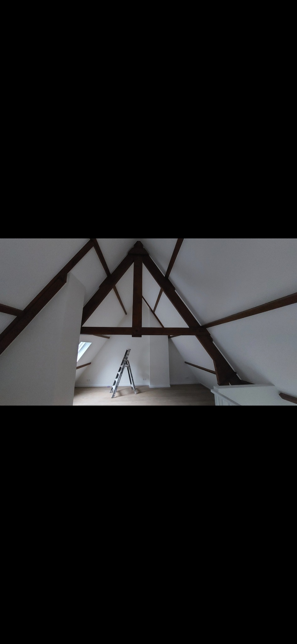 Poddasze po malowaniu na biało, widoczne drewniane belki stropowe, okno dachowe i drabina malarska. Świeżo pomalowane ściany i sufit.