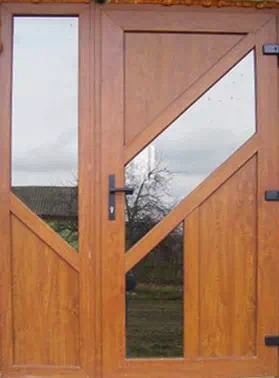 Brązowe, dwuskrzydłowe drzwi z asymetrycznymi szybami, widoczne z bliska, z fragmentem krajobrazu w tle. Nietypowy układ szyb nadaje drzwiom nowoczesny charakter.