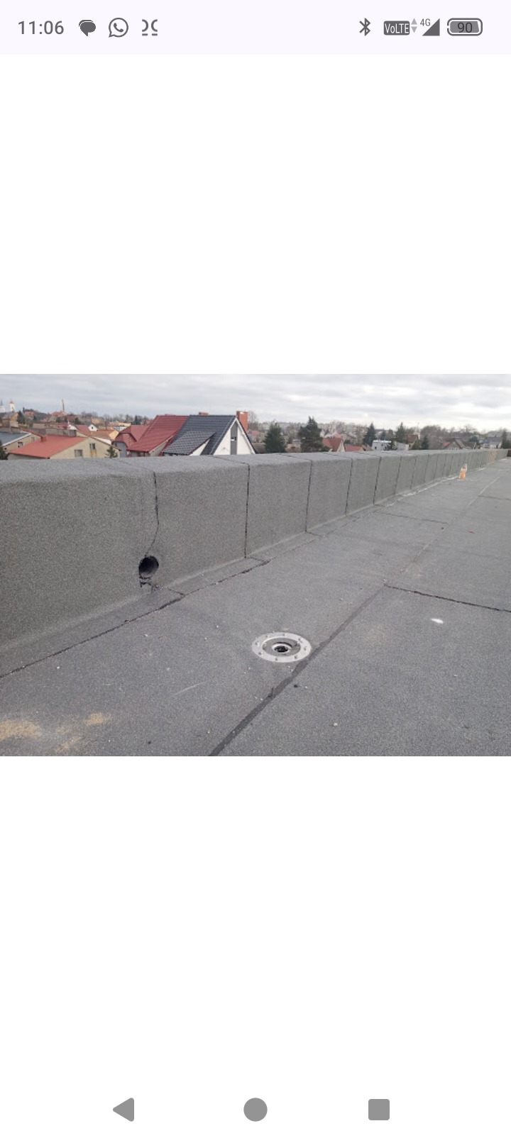 Szczegółowe ujęcie płaskiego dachu pokrytego papą termozgrzewalną z widocznym odpływem wody i otworem wentylacyjnym na tle zabudowy miejskiej.