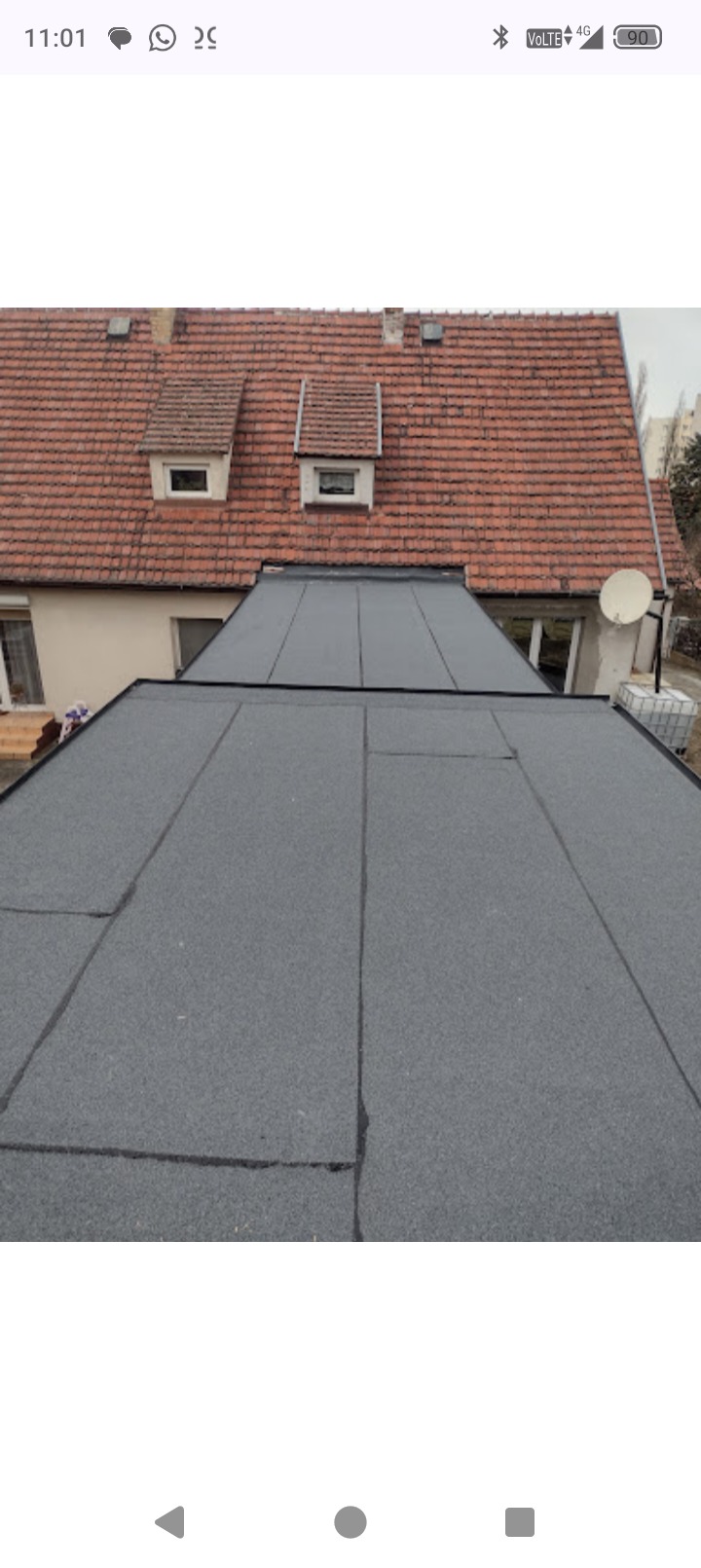 Szczelny dach płaski pokryty papą termozgrzewalną we Wrocławiu, widok z góry. W tle dach skośny z dachówki ceramicznej i okna połaciowe.