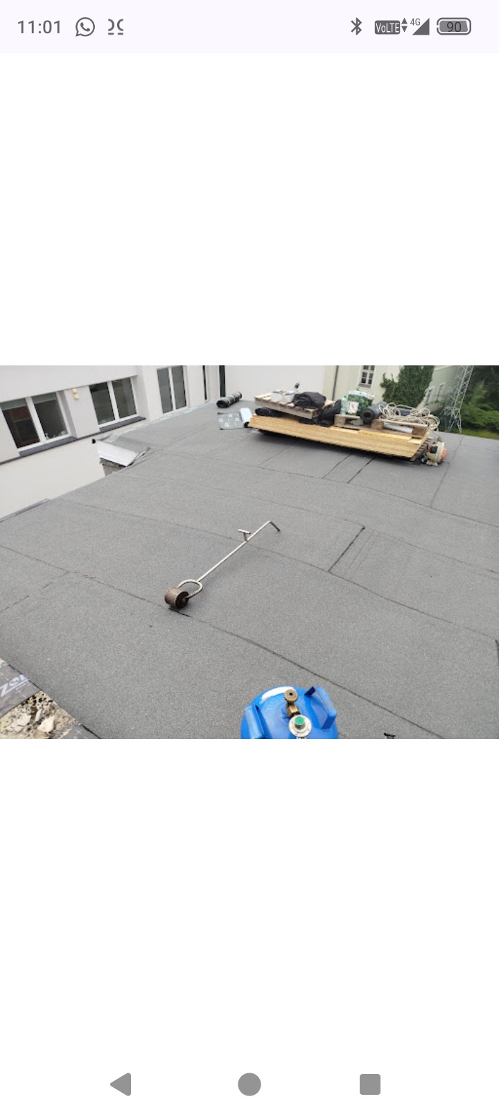 Wykończony dach płaski z papy termozgrzewalnej. Widoczny sprzęt dekarski, butla gazowa i narzędzia na dachu. Budynek w tle.