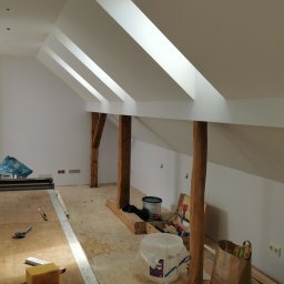 K1 - REMONTY & DOCIEPLENIA PRZEMYSŁAW KULKA - Białe poddasze ze skośnymi oknami dachowymi, drewnianymi belkami i narzędziami malarskimi. Widoczne przygotowania do malowania ścian.