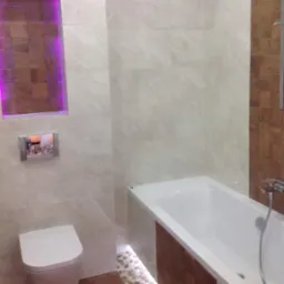 Wykończona łazienka z wanną, toaletą i mozaiką. Podświetlana wnęka z drewnianymi elementami. Płytki imitujące marmur na ścianach. Nowoczesny design.