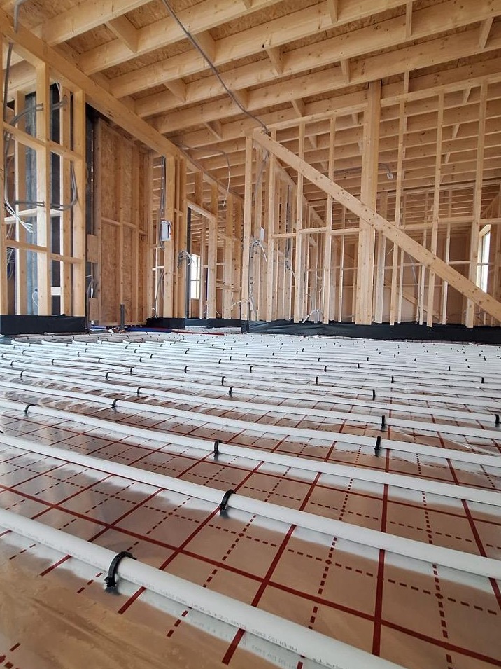 Wnętrze domu w konstrukcji szkieletowej z widoczną instalacją ogrzewania podłogowego, rury ułożone na folii z siatką, drewniana konstrukcja ścian i stropu.
