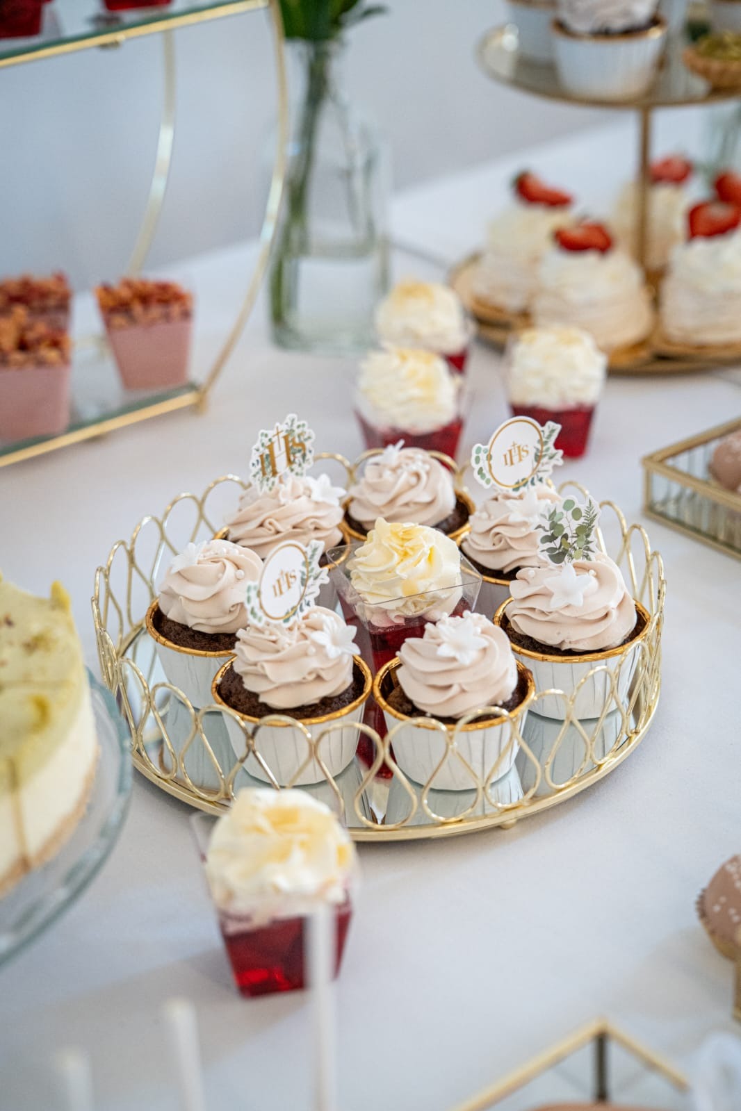 Elegancki złoty pater z babeczkami i deserami w galaretce, dekorowane motywami IHS, na białym stole. Słodki stół na uroczystość.