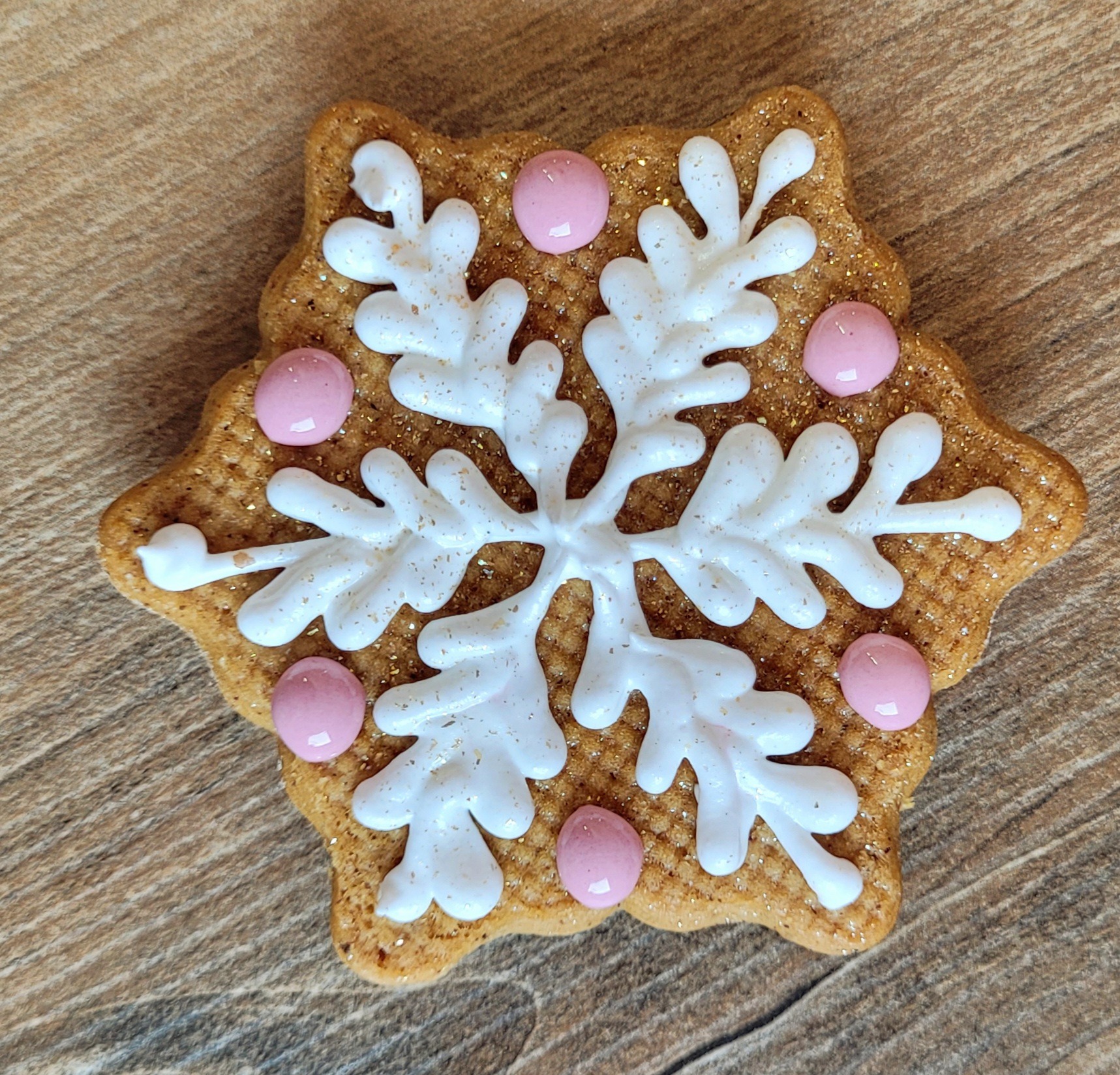 Piernikowy śnieżek z białym lukrem i różowymi koralikami na drewnianym tle. Dekoracja świąteczna, słodki upominek.