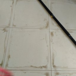 Anna Perfect - Białe, brudne płytki podłogowe z czarną rurą od odkurzacza i odczepioną końcówką. Widoczne ślady po zalaniach i zabrudzeniach w fugach.