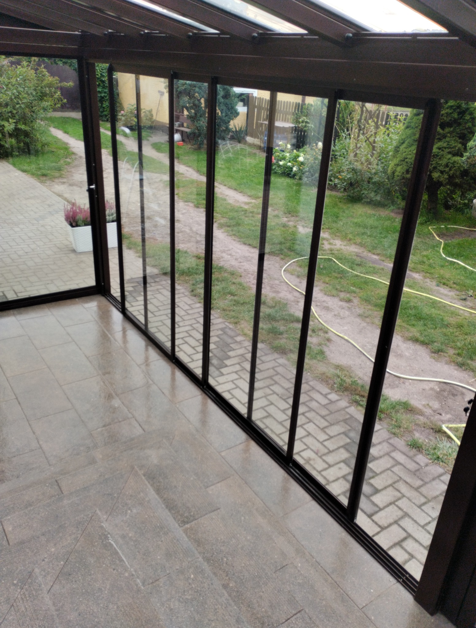 Szklana zabudowa tarasu z widokiem na ogród, po umyciu. Czyste szyby odbijają otoczenie, a na podłodze z płytek widoczne są delikatne refleksy światła.