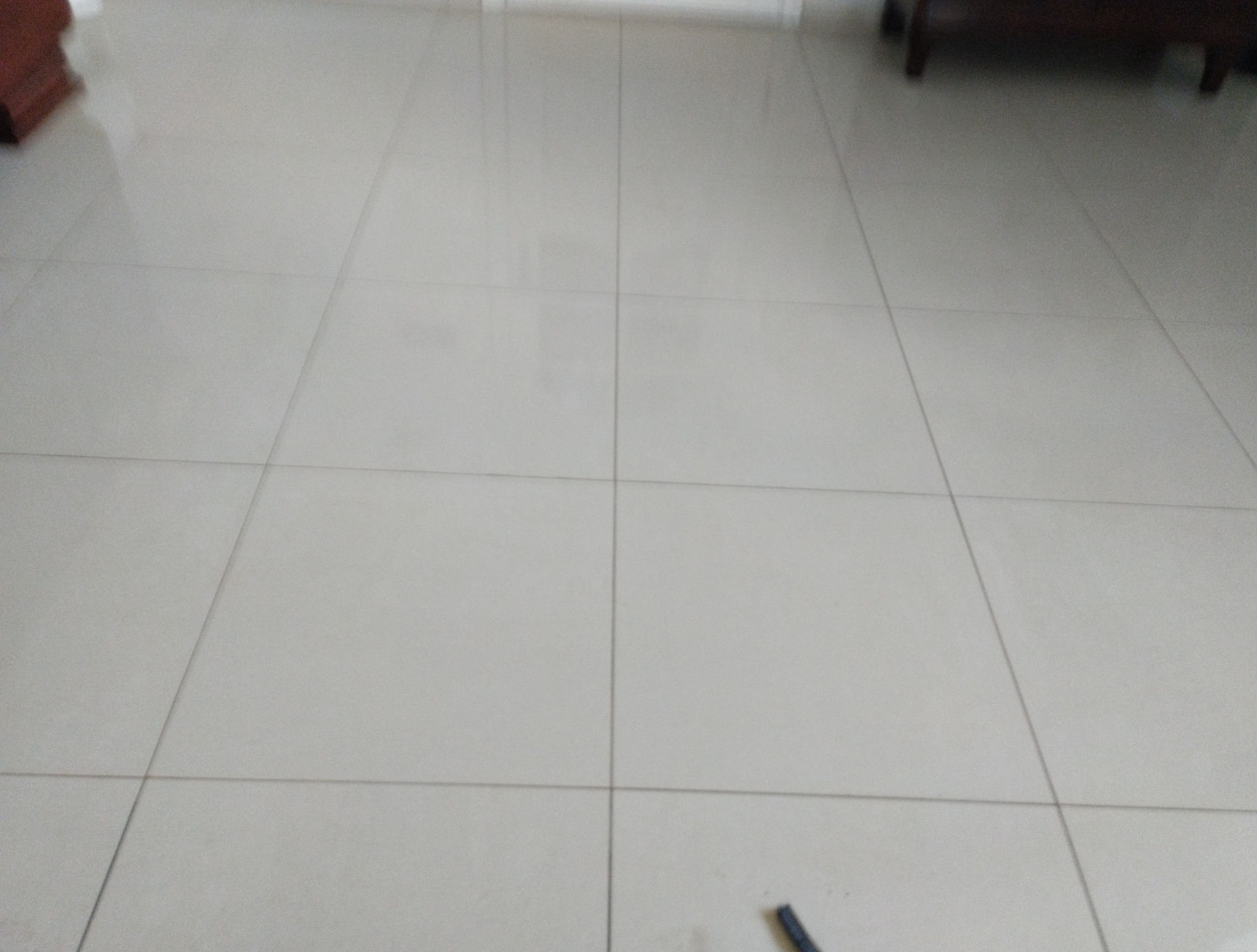 Błyszcząca, jasna podłoga z płytek po umyciu, widok z niskiej perspektywy. Minimalistyczne wnętrze z fragmentem mebla w tle. Czystość i odbicie światła.