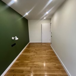 Yevhen Zatula - Korytarz po remoncie: drewniana podłoga, ściana w kolorze butelkowej zieleni z lampką, biała ściana z drzwiami. Widoczne oświetlenie sufitowe.