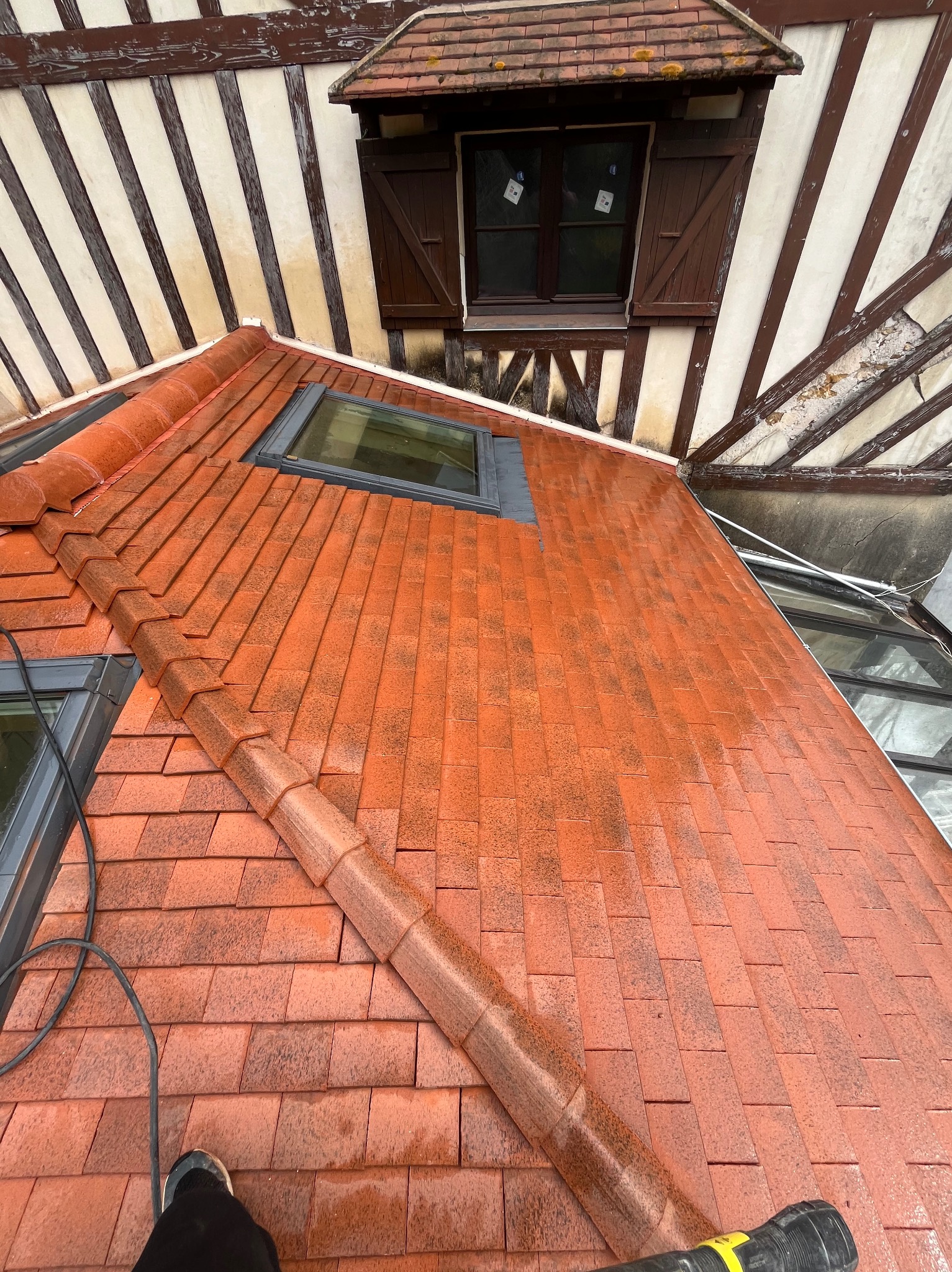 Czerwona dachówka po czyszczeniu, widoczne okna dachowe i fragment budynku z drewnianą konstrukcją szkieletową. Ślady wilgoci na powierzchni dachu.