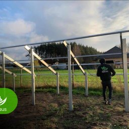 ECO Haus Daria Wiśniewska - Montaż konstrukcji wsporczej pod panele słoneczne na gruncie. Widoczny pracownik w firmowej bluzie i częściowo zamontowana konstrukcja z metalowych profili.