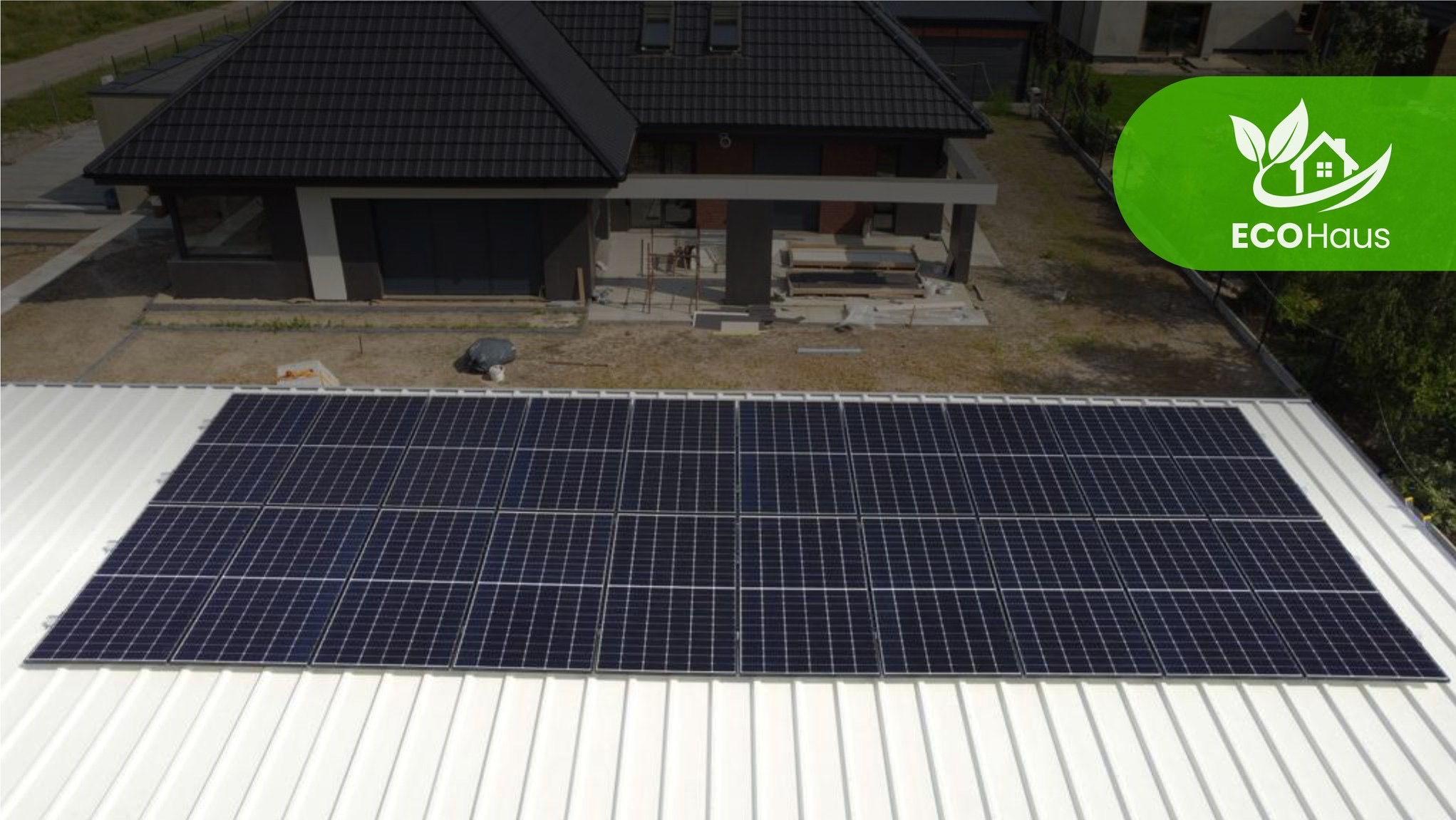 Instalacja paneli fotowoltaicznych na dachu domu jednorodzinnego w Więcborku. Widok z góry, panele w pełnym słońcu, w tle budynek z ciemnym dachem i logo firmy.