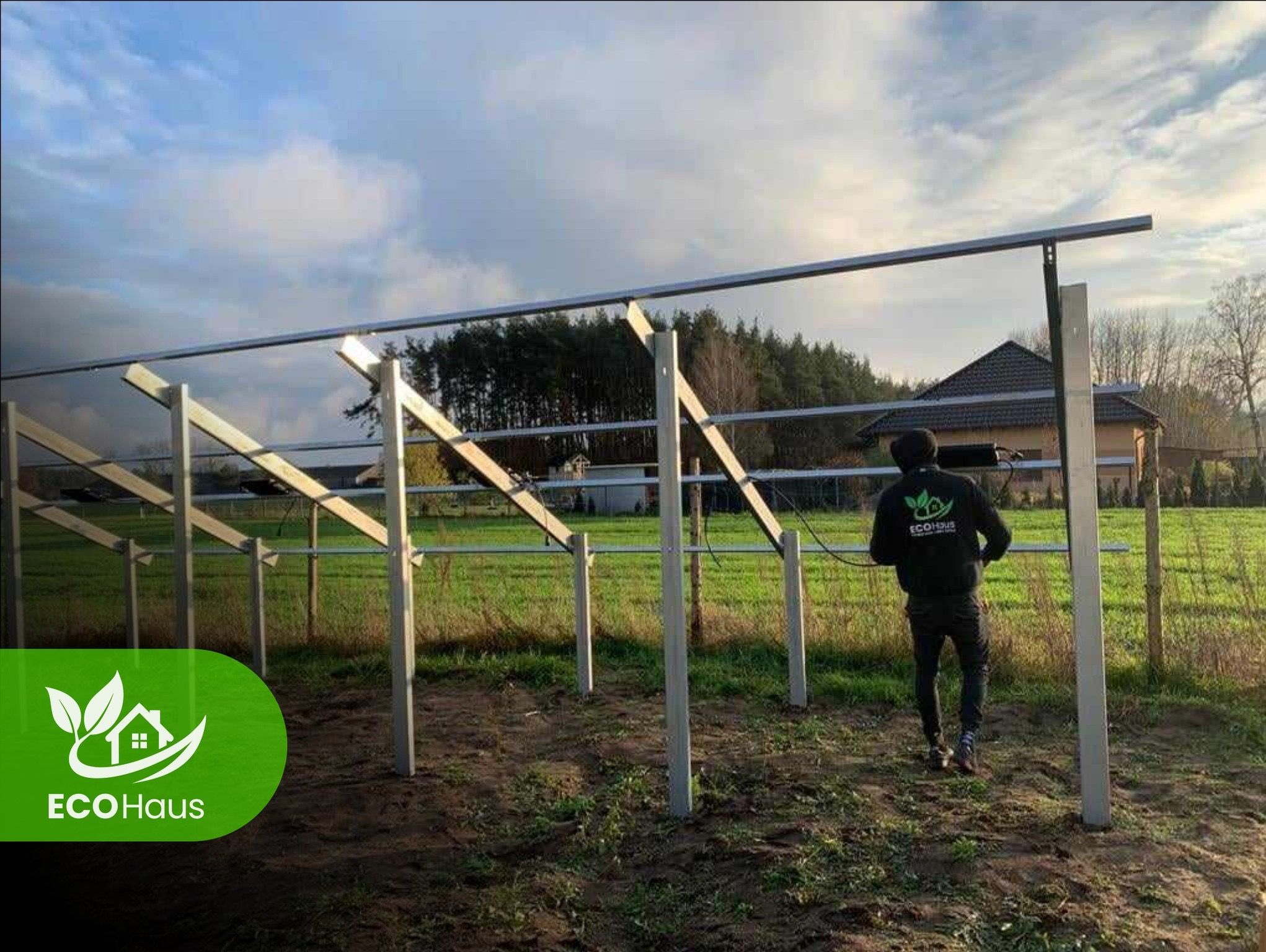 Montaż konstrukcji wsporczej pod panele słoneczne na gruncie. Widoczny pracownik w firmowej bluzie i częściowo zamontowana konstrukcja z metalowych profili.