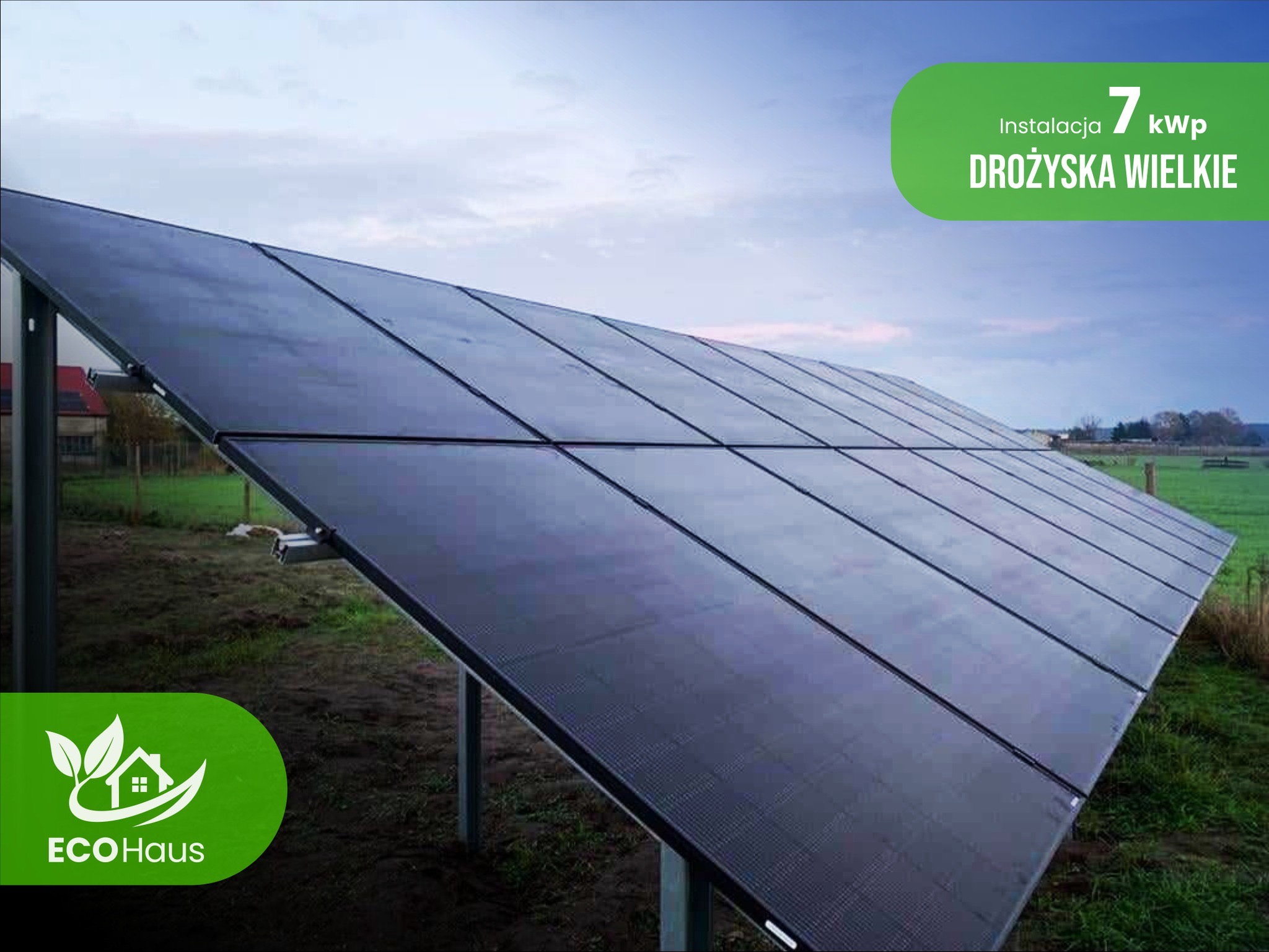 Instalacja fotowoltaiczna 7 kWp w Drożyskach Wielkich, zamontowana na gruncie. Widoczny logo EcoHaus. Ujęcie z dołu, pochmurne niebo w tle.