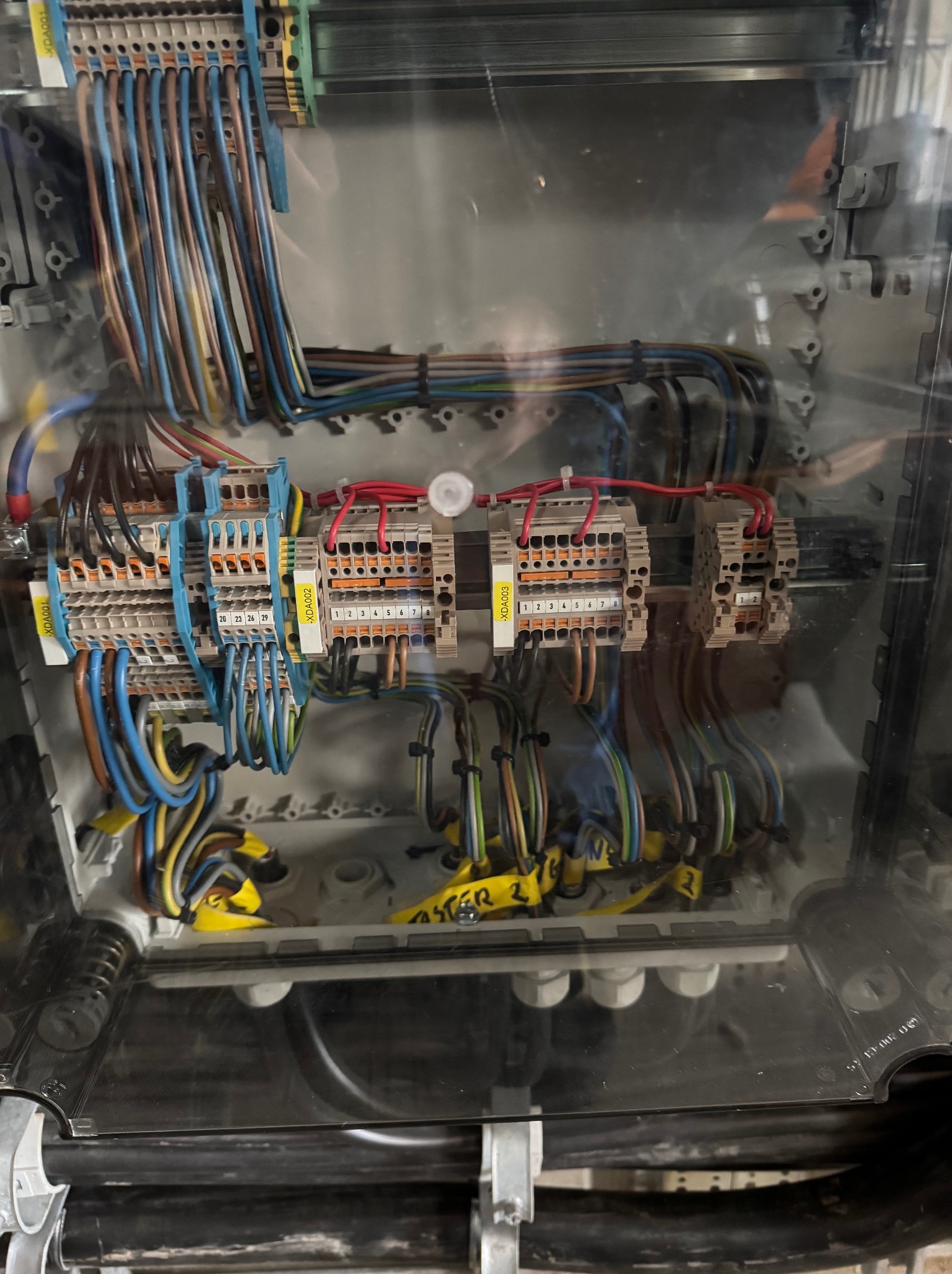 Rozdzielnica elektryczna z precyzyjnie ułożonymi przewodami o różnych kolorach, złączki opisane etykietami, widoczne elementy montażowe wewnątrz obudowy.