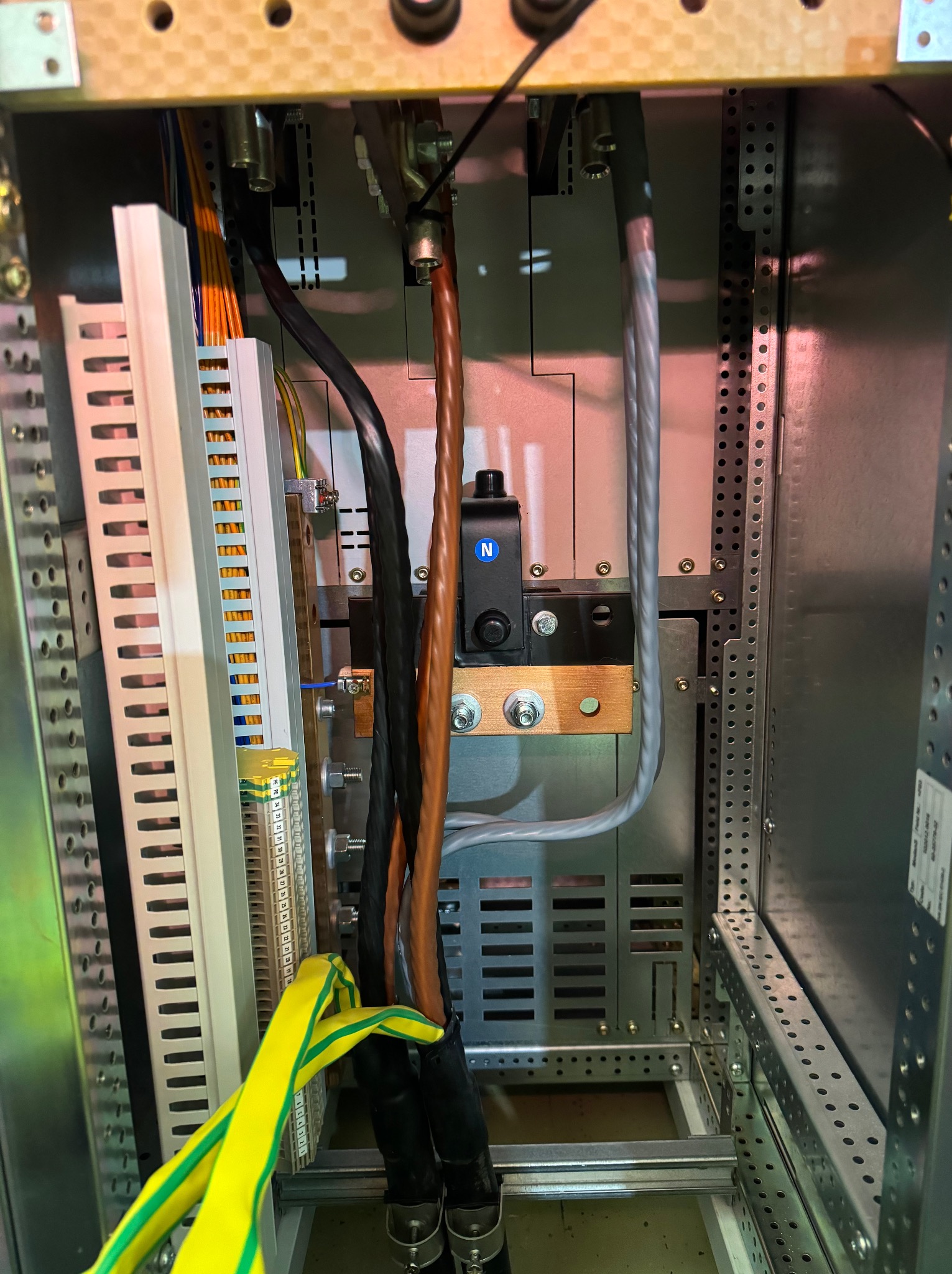 Wnętrze szafy elektrycznej z widocznymi przewodami, listwami zaciskowymi i elementami montażowymi. Kabel ochronny żółto-zielony. Widoczne złącza i zabezpieczenia.