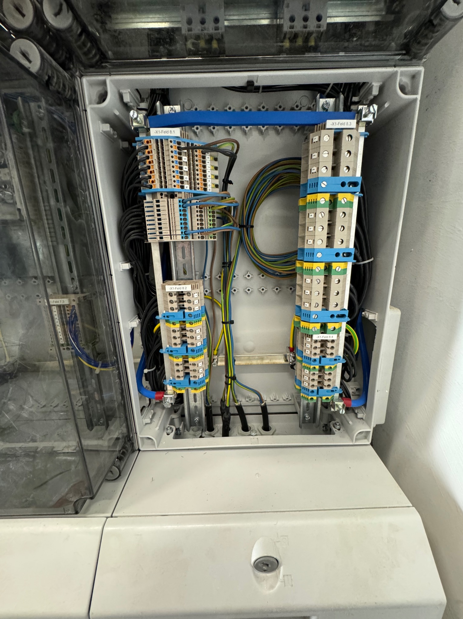 Otwarta skrzynka elektryczna z widocznymi przewodami, złączkami i elementami montażowymi. Instalacja wewnątrz skrzynki uporządkowana, przewody w różnych kolorach.