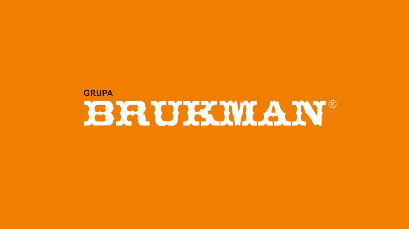 Logo firmy Grupa Brukman na pomarańczowym tle. Nazwa firmy w białym kolorze, stylizowana czcionka. Widoczny znak zastrzeżony.
