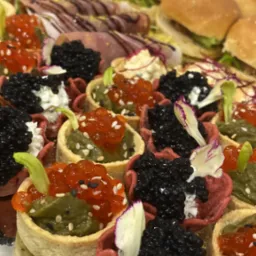 Eleganckie przekąski cateringowe: mini tartaletki z kawiorem i pastą, kanapki z szynką i sałatą, ułożone na srebrnej tacy. Idealne na wykwintne przyjęcie.