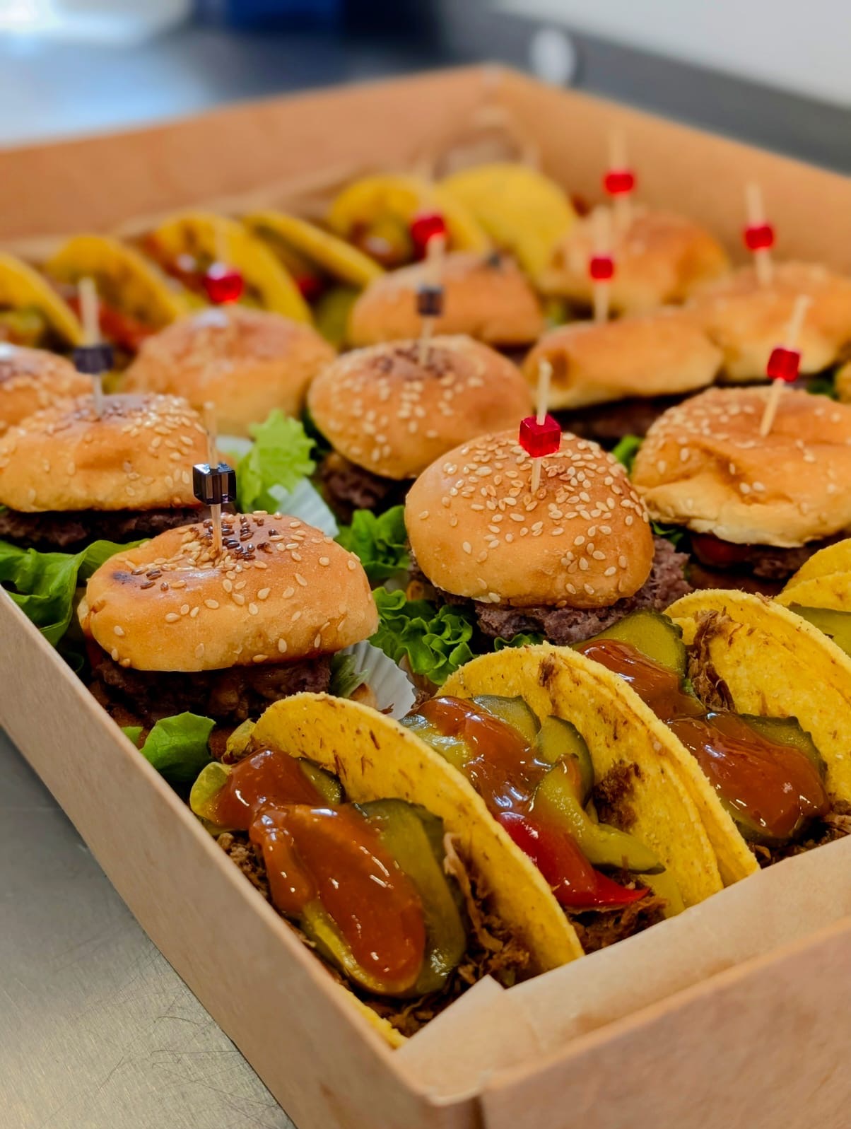 Zestaw mini burgerów i tacos w kartonowym pudełku cateringowym. Burgery z sezamem, tacos z sosem i ogórkiem. Idealne na imprezy firmowe i catering świąteczny.