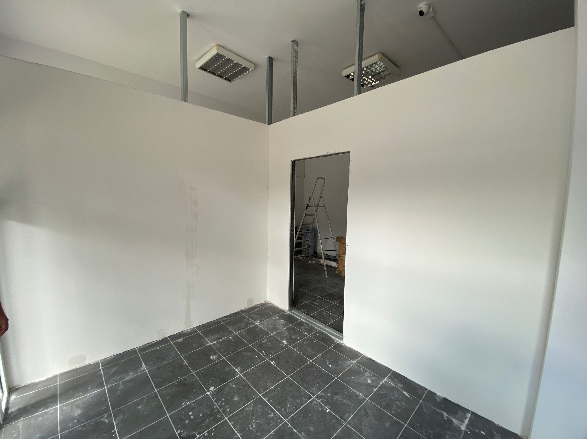 Wnętrze po remoncie w Lublinie: białe ściany, ciemna podłoga z płytek, widoczne elementy konstrukcji sufitu podwieszanego i drabina w tle.