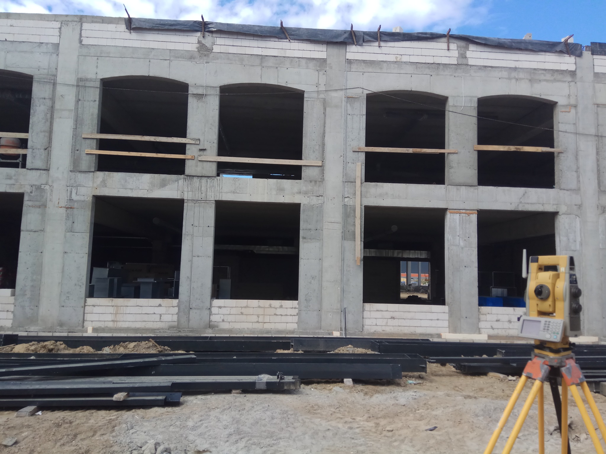 Surowy stan budynku z betonu komórkowego z widocznym teodolitem na statywie, sugerującym prace geodezyjne na placu budowy.