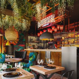 REDLICKI STUDIO Piotr Redlisz-Redlicki - Eklektyczny wystrój baru z roślinami, neonem Beefeater, drewnianymi elementami i krzesłami w pawie pióra. Unikalne lampy i zastawa stołowa dodają charakteru.