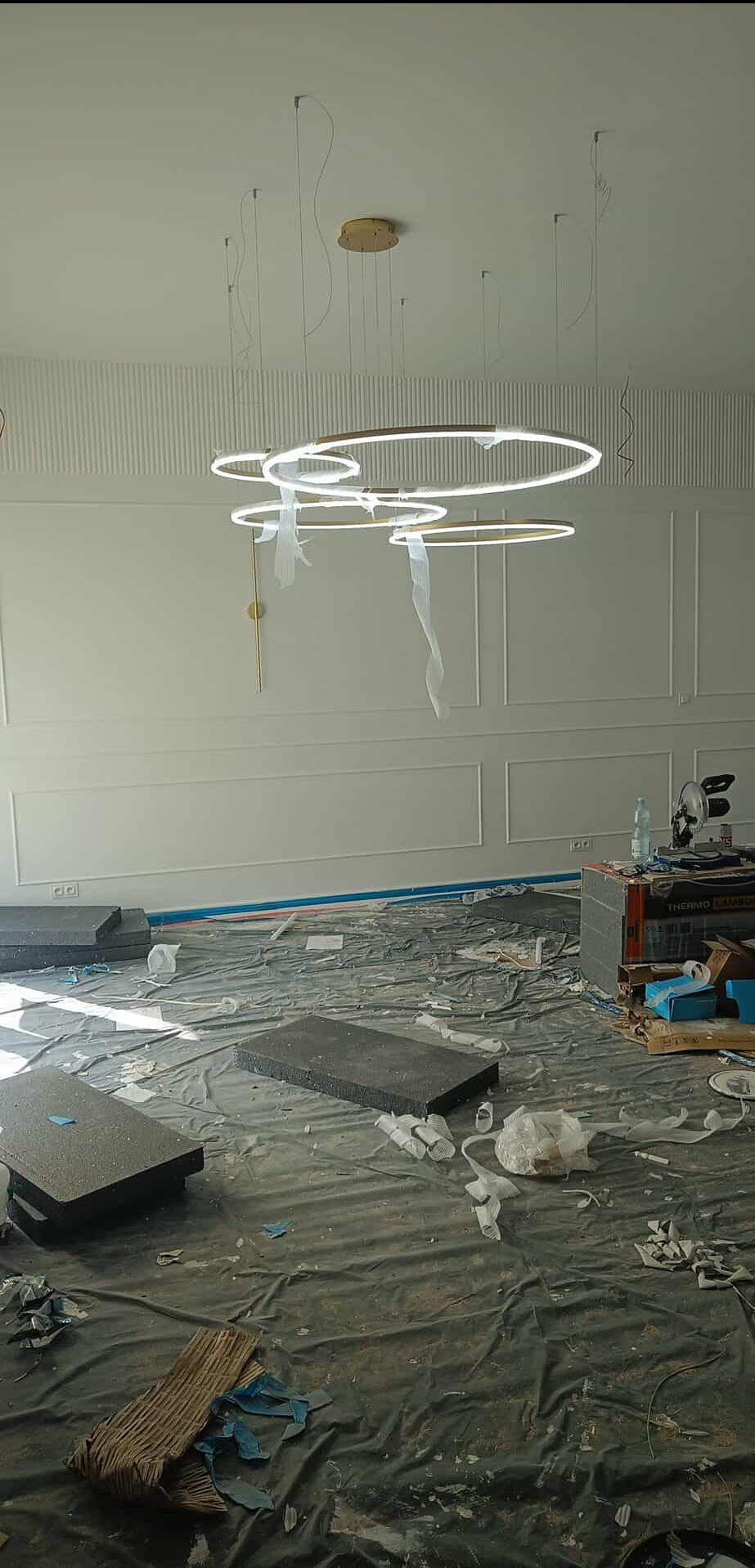 Montaż nowoczesnej lampy pierścieniowej w jasnym wnętrzu z dekoracyjną sztukaterią. Widoczne kable i elementy montażowe, sugerujące etap instalacji.