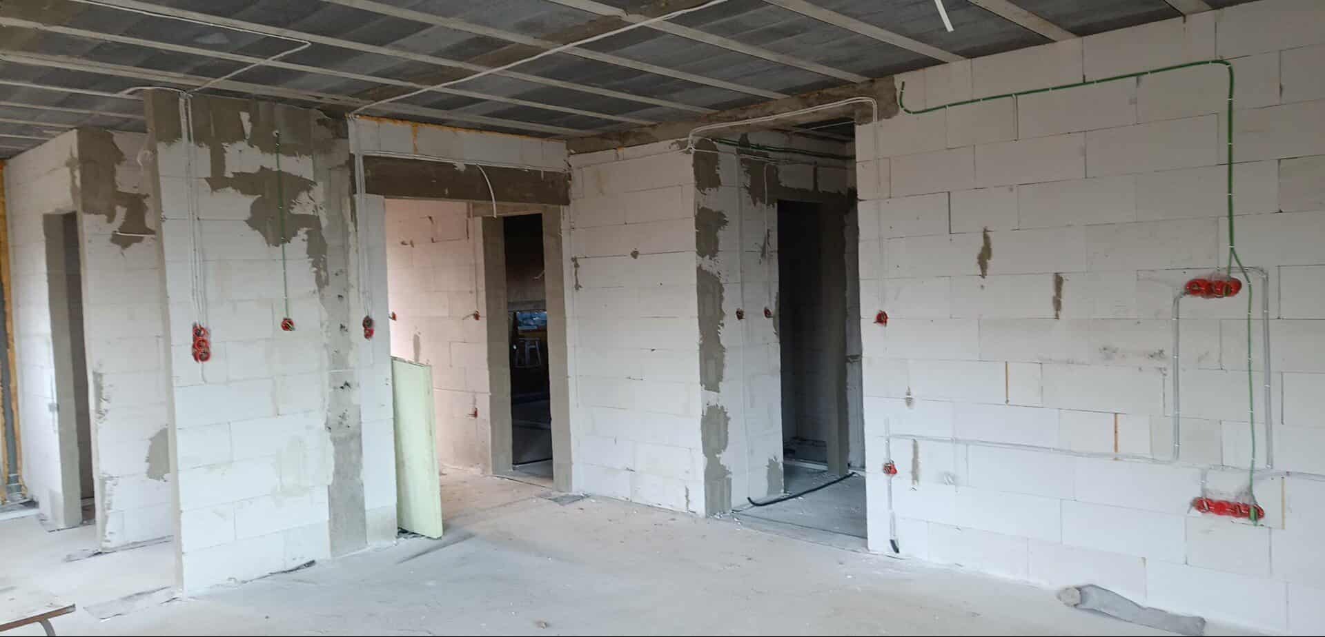 Wnętrze w trakcie prac instalacyjnych: widoczne ściany z betonu komórkowego, rozprowadzone przewody elektryczne w peszlach i puszki pod gniazdka. Surowy stan wykończenia.