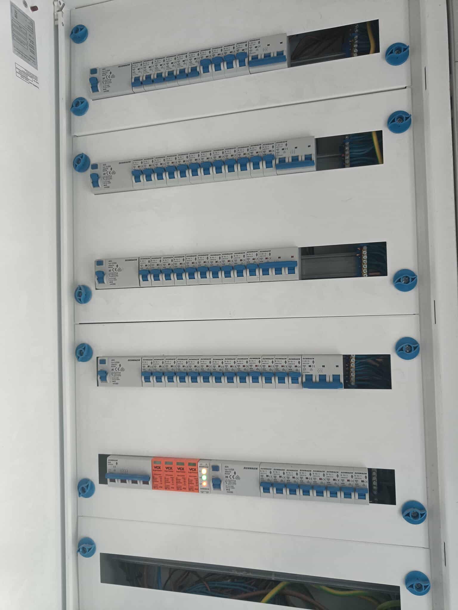 Rozdzielnica elektryczna z bezpiecznikami i przewodami, widoczne elementy instalacji, zabezpieczenia i okablowanie wewnątrz szafki.